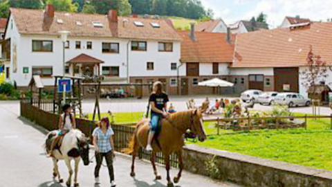 Pferde mit Personen vor dem Ferienhofgebäuden